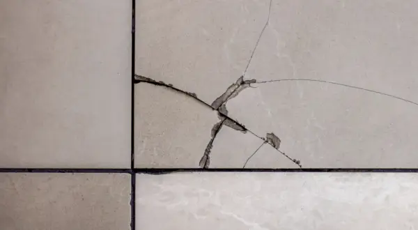 Gros plan sur un carrelage beige avec une fissure traversant plusieurs carreaux, révélant la couche inférieure.