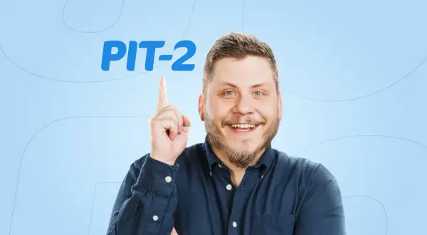 Uśmiechnięty mężczyzna w granatowej koszuli wskazuje palcem na napis PIT-2.