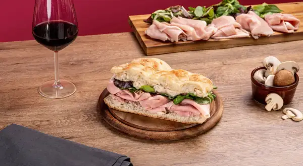 Une délicieuse schiacciata garnie de jambon et de verdure, accompagnée d'un verre de vin rouge et de champignons frais.