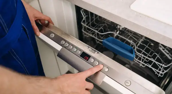 Ręka naciska przycisk na panelu zmywarki Whirlpool, pokazując, jak zresetować zmywarkę Whirlpool.