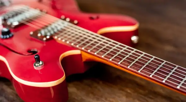 Czerwona gitara elektryczna na drewnianym tle. Idealna do nauki gry na gitarze elektrycznej.