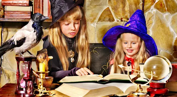 Dwie dziewczynki w strojach czarownic tworzą magiczne prace plastyczne na Andrzejki, otoczone tajemniczymi rekwizytami.