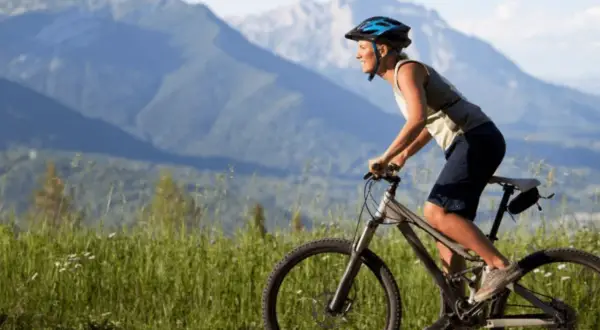 Ciclista sonriente pedalea por un camino de grava con montañas al fondo. Una aventura de pirinexus gravel.