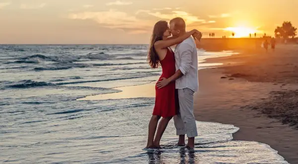 Para świętuje 20 lat razem, całując się na plaży o zachodzie słońca.