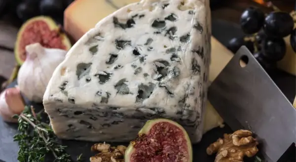 Un trozo de queso azul, con sus vetas verdes, parece un queso que huele mal. Acompañado de higos, nueces y ajo.