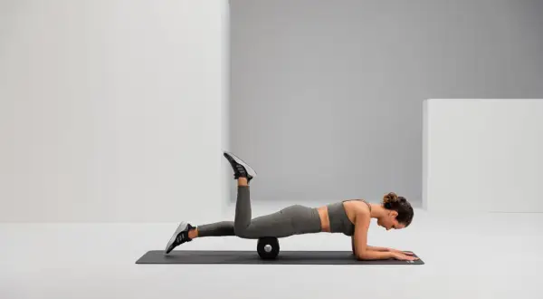 Frau auf einer Matte mit Foam Roller unter dem Oberschenkel, um Hohlkreuz wegtrainieren.