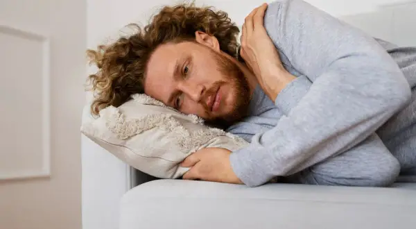 Uomo con capelli ricci e barba sdraiato su un divano, che riflette sulla necessità di esercizi per superare l'agorafobia.