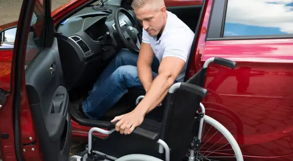 Mann mit Rollstuhl steigt in rotes Auto. Dies illustriert die behinderungsbedingte Fahrtkostenpauschale.