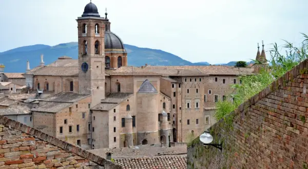 La maestosa corte di Urbino, con il suo campanile e la cupola, si staglia contro le colline.