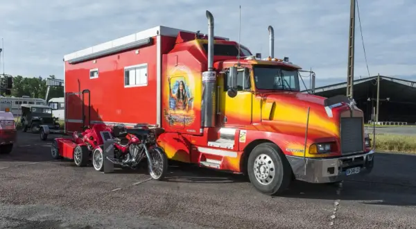 Un poid lourd américain rouge et jaune, customisé avec une peinture de femme amérindienne, est garé à côté d'une moto rouge.