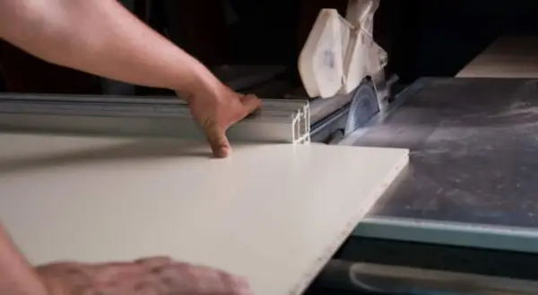 Precyzyjne cięcie płyty MDF na pile stołowej. Ręce stolarza prowadzą materiał do obracającej się tarczy.