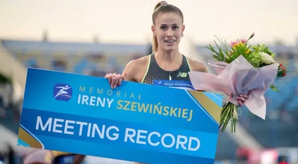 Uśmiechnięta lekkoatletka z bukietem kwiatów trzyma tablicę "MEETING RECORD" z logo memoriału Ireny Szewińskiej.
