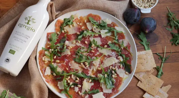 Delicioso carpaccio de higos con jamón serrano, piñones, rúcula y lascas de queso. Un plato ligero y lleno de sabor.