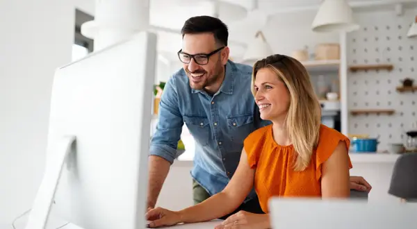Coppia sorridente davanti al computer, scopre come funziona la banca ore per ottimizzare il lavoro.
