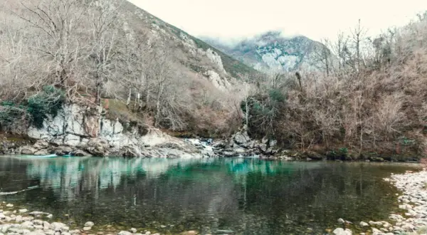 El río turquesa fluye sereno, reflejando árboles desnudos y montañas neblinosas. Un paisaje que evoca la paz de la olla de San Vicente.