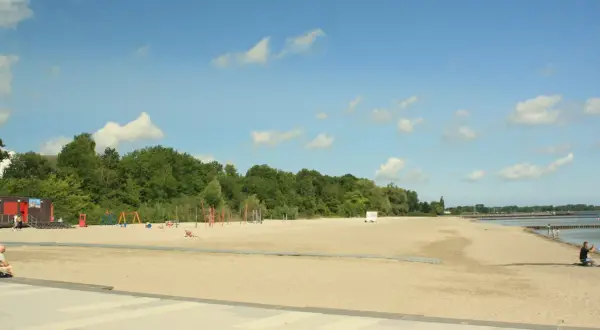 Sonniger **Stralsund Strand** mit Spielplatz, Liegewiese und Blick aufs Wasser. Ein Mann macht ein Foto.