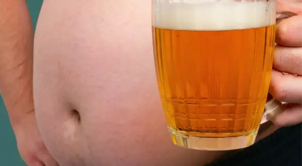 Ein Bierbauch ist da, weil Bier dick macht. Ein Mann hält ein Glas Bier vor seinem Bauch.