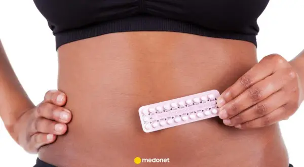 Kobieta trzyma blister tabletek antykoncepcyjnych, np. Belara, na brzuchu.