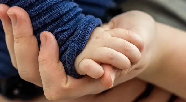 Eine Hand hält zart die kleine Hand eines Babys. Die Frage, warum hilft Gott nicht bei Depressionen, hallt in dieser Geste der Verbundenheit wider.