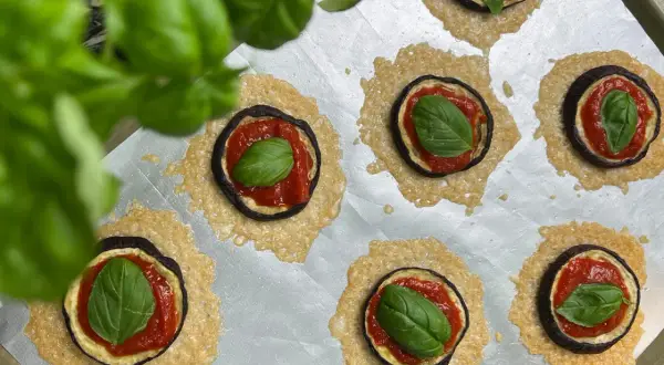 Kleine Aubergine-Pizza-Häppchen mit Tomatensoße, Käse und frischem Basilikum auf einem Backblech.