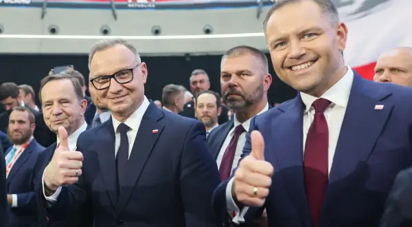 Dwóch mężczyzn w garniturach, jeden z nich pokazuje kciuk w górę. W tle widać napis CPAC Poland. Długość kadencji prezydenta jest tematem dyskusji.