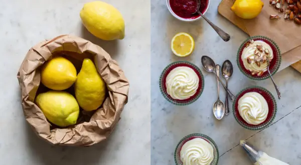 Färska citroner i en papperspåse bredvid färdiga citron dessert i glasbägare, toppade med vispgrädde och mandlar.