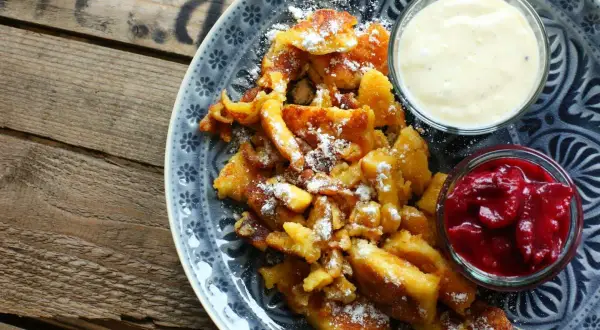 Ein köstlicher Kaiserschmarrn, bestäubt mit Puderzucker, serviert mit Apfelmus und Vanillesauce. Ein einfaches Rezept für Genuss.