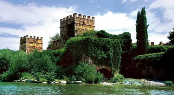 Antiche gualchiere di Remole, torri medievali immerse nel verde, si specchiano in un fiume tranquillo sotto un cielo nuvoloso.