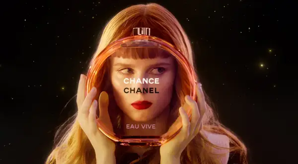 Kobieta z rudymi włosami trzyma okrągłą butelkę perfum Chanel Chance Eau Vive.