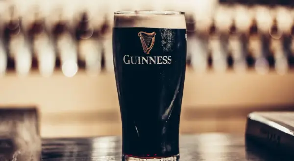Szklanka ciemnego piwa stout Guinness z pianką na wierzchu, na drewnianym blacie.
