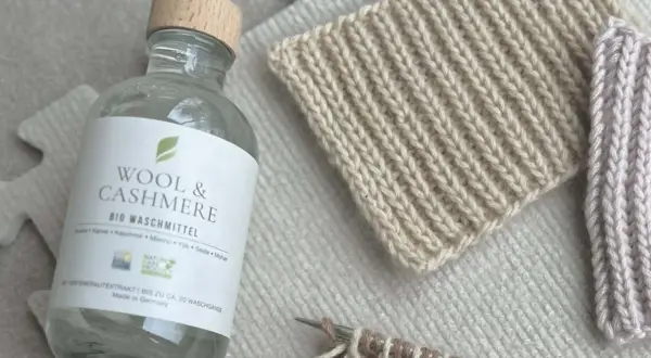 Flasche "Wool & Cashmere" Bio-Waschmittel neben gestrickten Proben. Ideal für die Frage: Pullover waschen welches Programm?