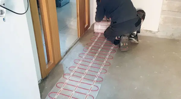 Instalator układa matę grzewczą, przygotowując ogrzewanie podłogowe.