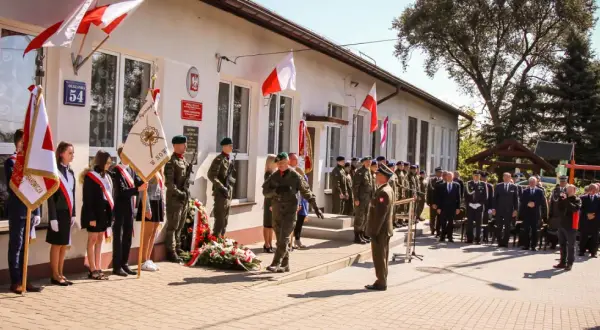 Uroczystość przed budynkiem szkoły z udziałem wojska, uczniów i gości.