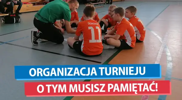 Trener w zielonej koszulce tłumaczy dzieciom w pomarańczowych strojach, jak zorganizować turniej piłki nożnej.