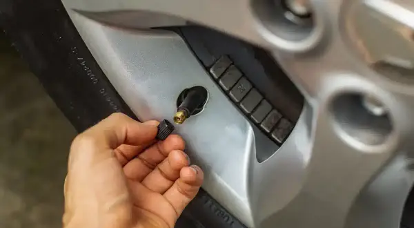Main tenant le capuchon d'une valve pneu qui fuit, révélant le mécanisme de la valve.