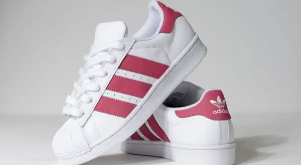 Białe buty Adidas Superstar z różowymi paskami i logo.