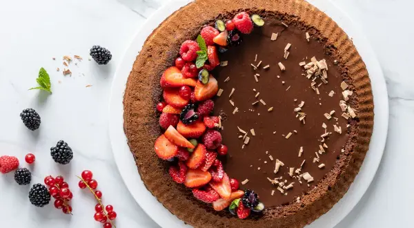 Torta Lindt al cioccolato fondente, decorata con fragole, lamponi, ribes e mirtilli. Un capolavoro goloso.