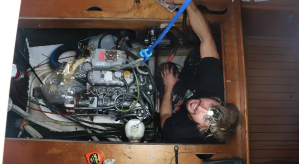 Uomo con torcia frontale lavora sul motore di una barca, tra tubi e cavi. Il calcolo carburante nautica è fondamentale per la navigazione.