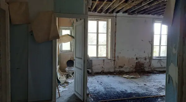 Intérieur délabré d'une maison abandonnée dans les Ardennes, avec un papier peint déchiré, un plafond effondré et une vieille cuvette de toilette. Urbex Ardennes.