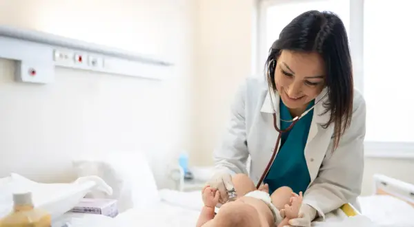 Uśmiechnięty neonatolog bada noworodka stetoskopem.