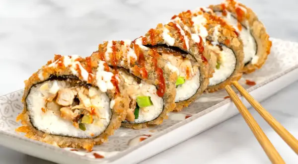 Knusprig frittiertes Sushi mit Hühnchen und Gemüse, beträufelt mit Saucen. Ein köstlicher Genuss!