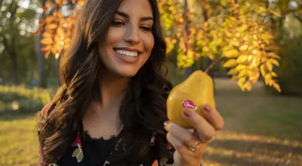 Donna sorridente tiene una pera gialla, uno dei cibi che fanno fare la cacca subito, in un parco autunnale.