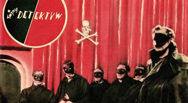 Grupa zamaskowanych postaci w czarnych strojach, na czerwonym tle z symbolem czaszki i piszczeli. Może to być scena z tajemniczej czarnej mszy.