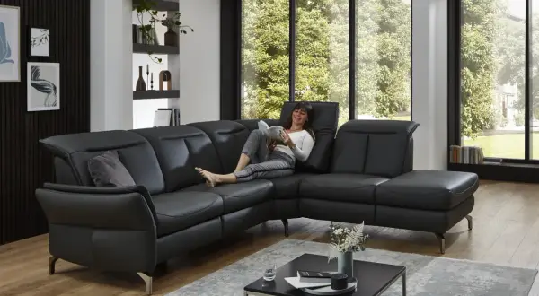 Frau liest auf schwarzem Ledersofa. Dieses Leder ist am robustesten und pflegeleicht, ideal für den Alltag.