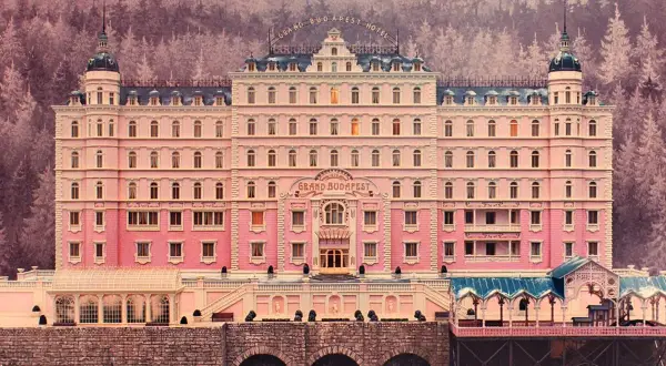 A grand pink hotel with a distinct Wes Anderson aesthetic, nestled in a snowy, purple-hued forest.
