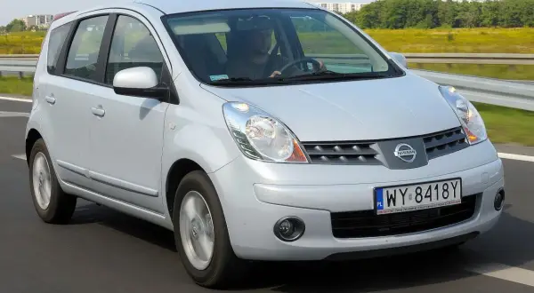 Srebrny Nissan Note na drodze. Kierowca w czapce prowadzi auto. Wiele osób szuka nissan note opinie przed zakupem.