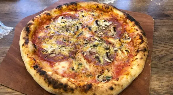 Chrupiąca pizza z pieczarkami i salami na drewnianej desce.
