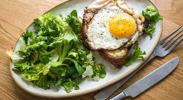 Ein herzhafter Croque Madame mit Spiegelei, Käse und Toast, serviert mit frischem Salat.