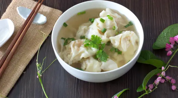 Aromaticzne chińskie pierożki w bulionie, ozdobione szczypiorkiem i kolendrą, gotowe do spożycia z pałeczkami.