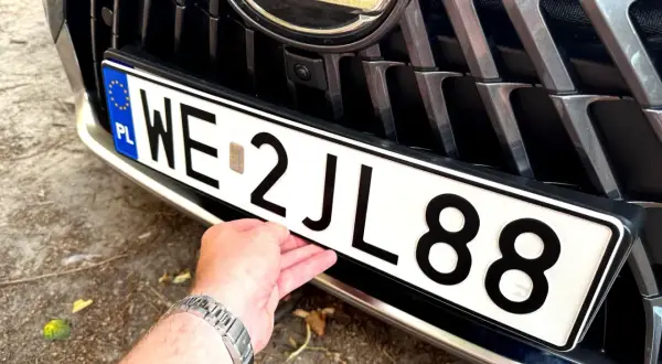 Dłoń poprawia tablicę rejestracyjną z numerem WE 2JL88, przygotowując wniosek o rejestrację pojazdu.
